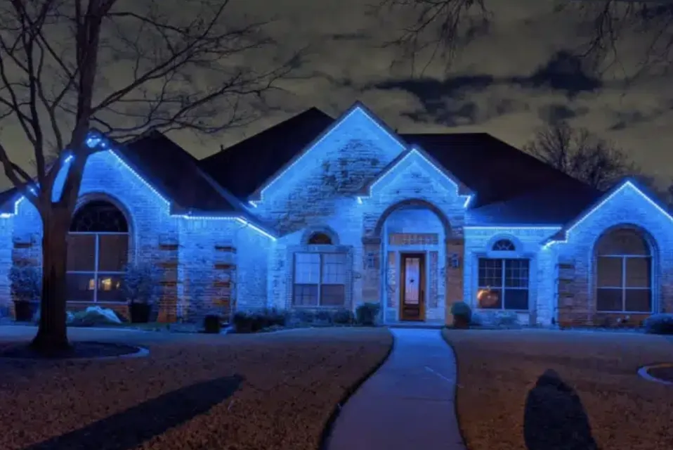 Stone-front home lit in cool blue along the roof and entry.