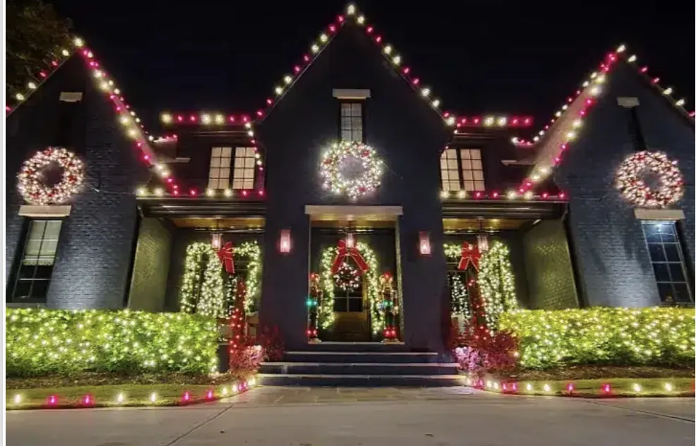 Dark brick house dressed in red and white lights with wreaths hung across the front.