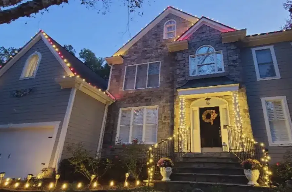 Gray stone home at dusk with red lights on the roof peaks and a lit front entry.