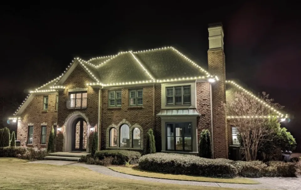 Big brick house with a chimney, clipped front shrubs and a full warm white roofline.