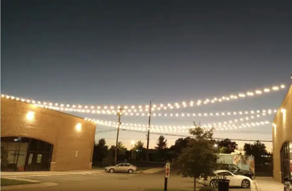 Strings of white lights crossing a street of brick storefronts after dark.