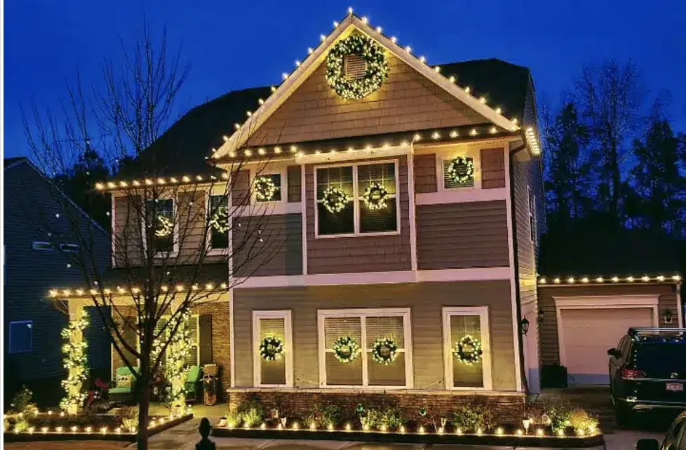 Two-story home at dusk with clean roofline lights and a wreath on each front window.