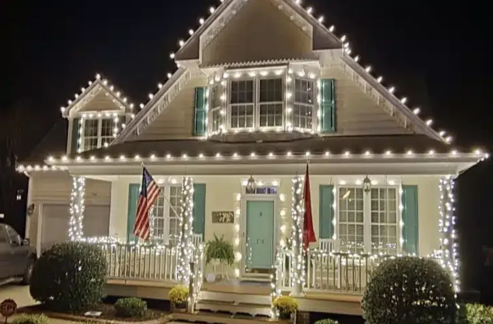 White cottage with teal shutters, a flag by the door and a neat string of lights along the eave.