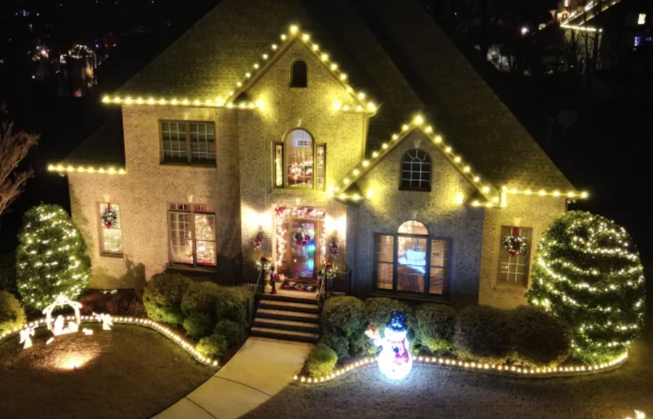 Brick house seen from above with wreaths, wrapped shrubs and lights lining the front walk.